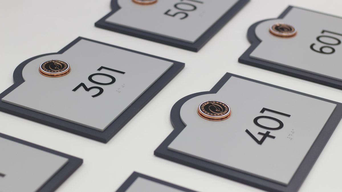 Custom-shaped gray unit ID signs with copper accent medallions for multifamily property showing series 300-400