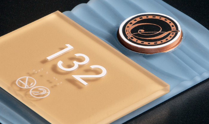 Gold-finished thermoformed unit ID sign with decorative copper medallion accent for luxury multifamily